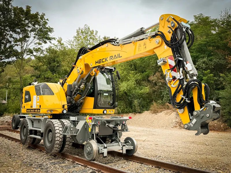 Liebherr A 922 Rail mit HECK RAIL-Schriftzug am Ausleger, auf dem Gleis vor Bäumen