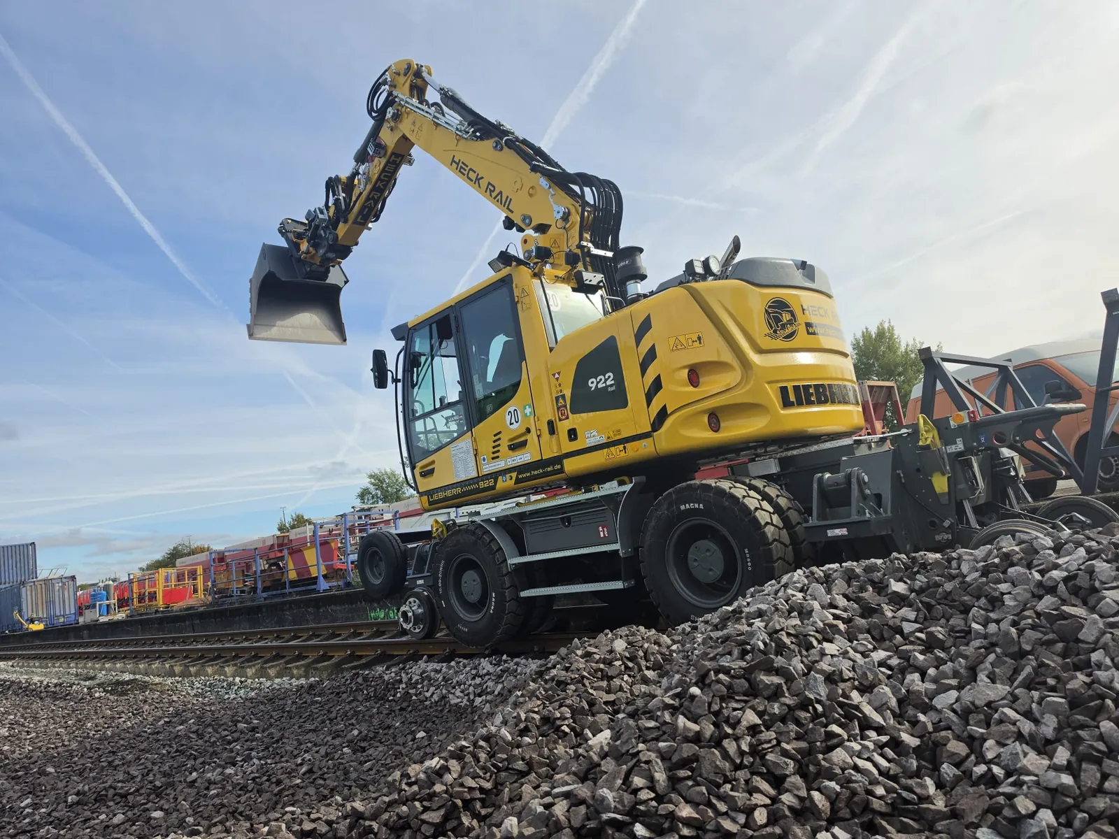 Liebherr 922 Rail von HECK RAIL auf dem Gleis, Löffel angehoben, vorn Schotter